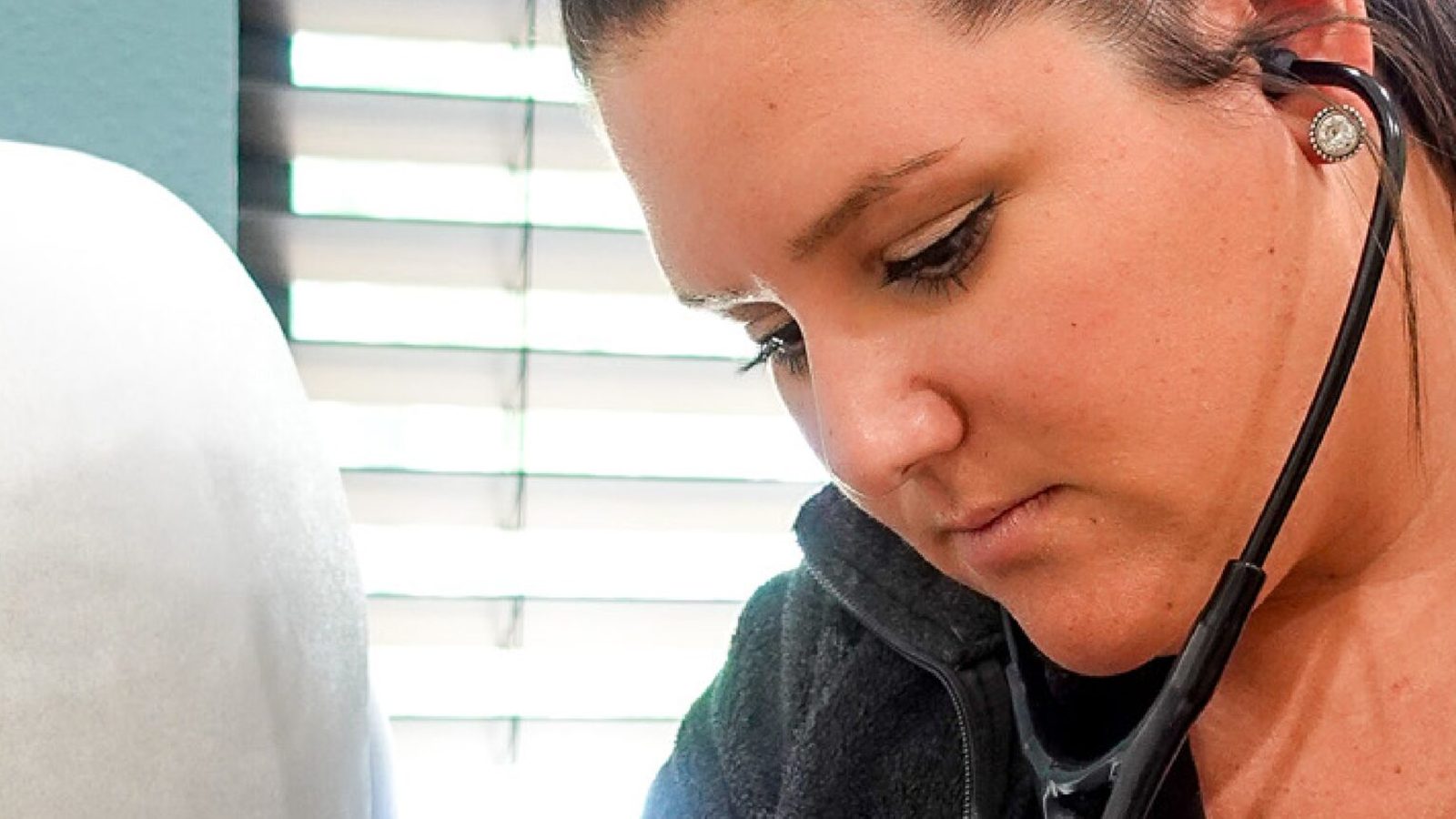 A nurse practitioner listening to a patient's heart with a stethoscope